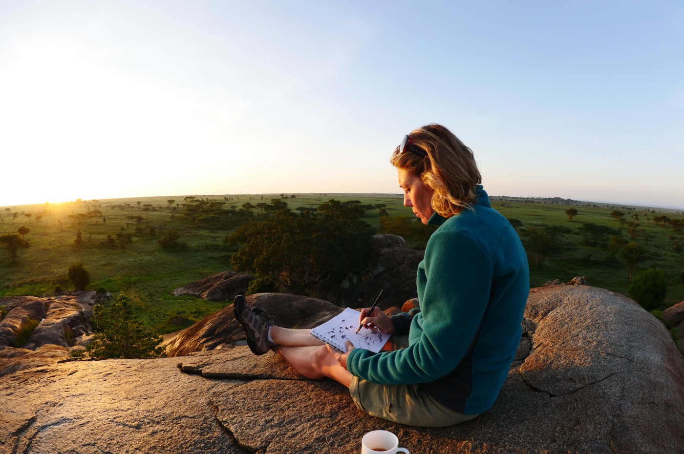 Person with a coffee cup drawing with a view over the savannah Wayo Walking Safari Camp, Serengeti, Tanzania