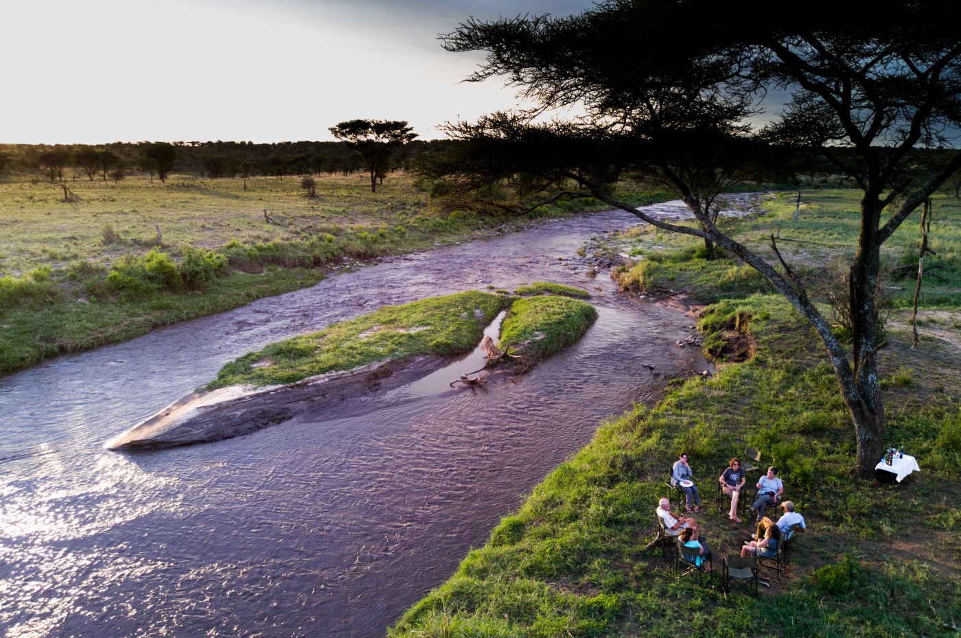People sitting next to the river in the bush at Wayo Walking Safari Camp, Serengeti, Tanzania